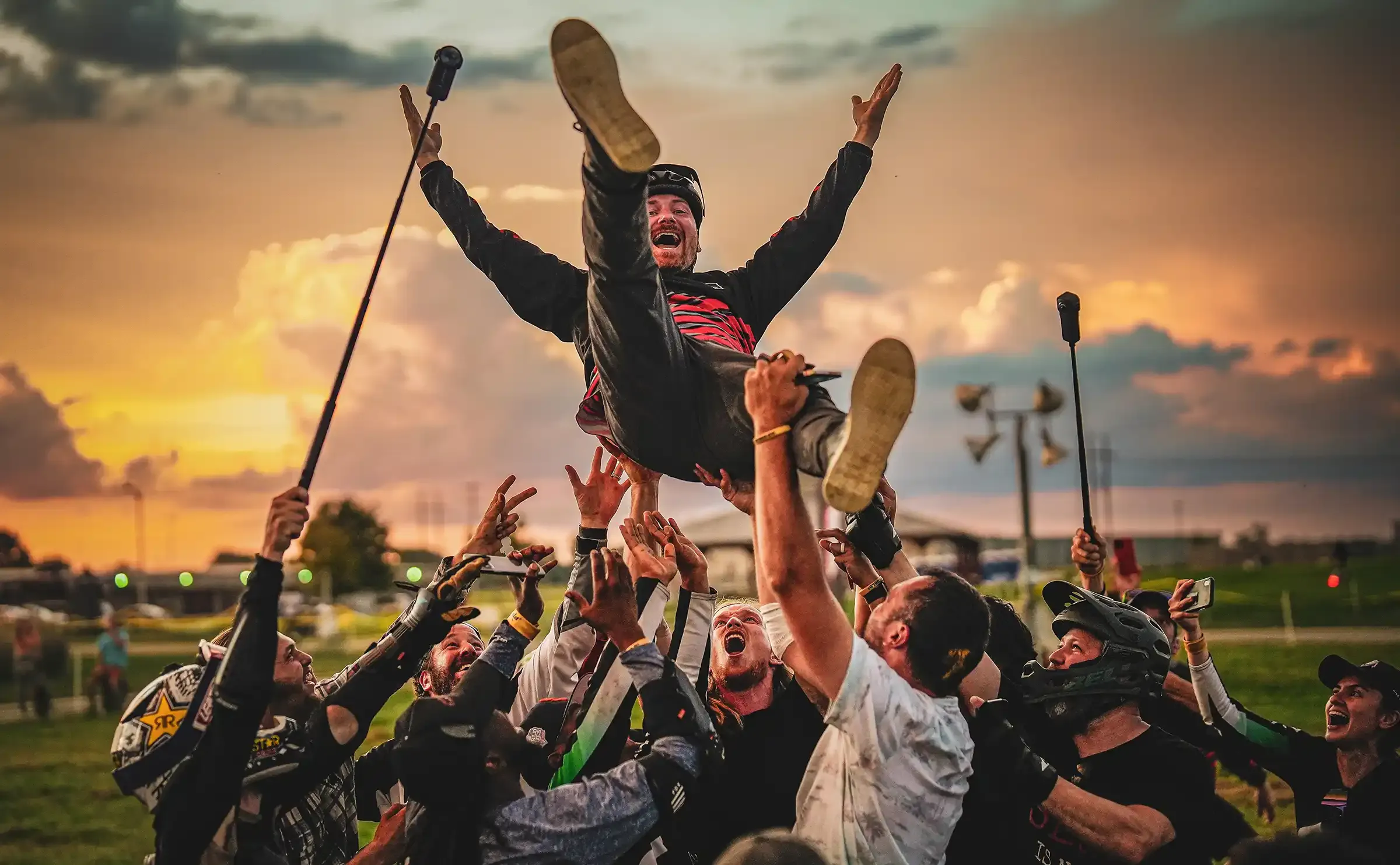 Riders in protective gear lift a cheering rider into the air at sunset