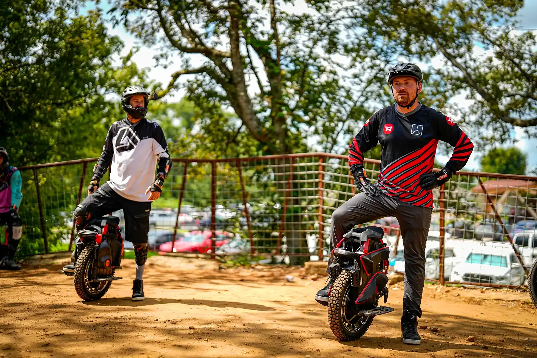 Two riders in motocross gear stand beside their electric unicycles on a dirt trail