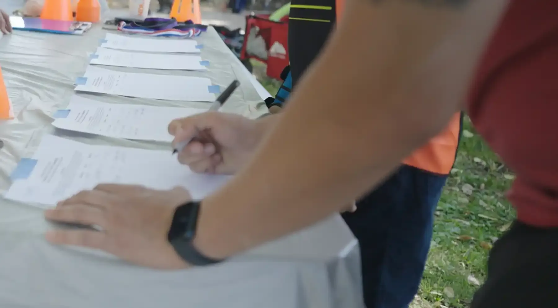 A person signs paper forms on a registration table