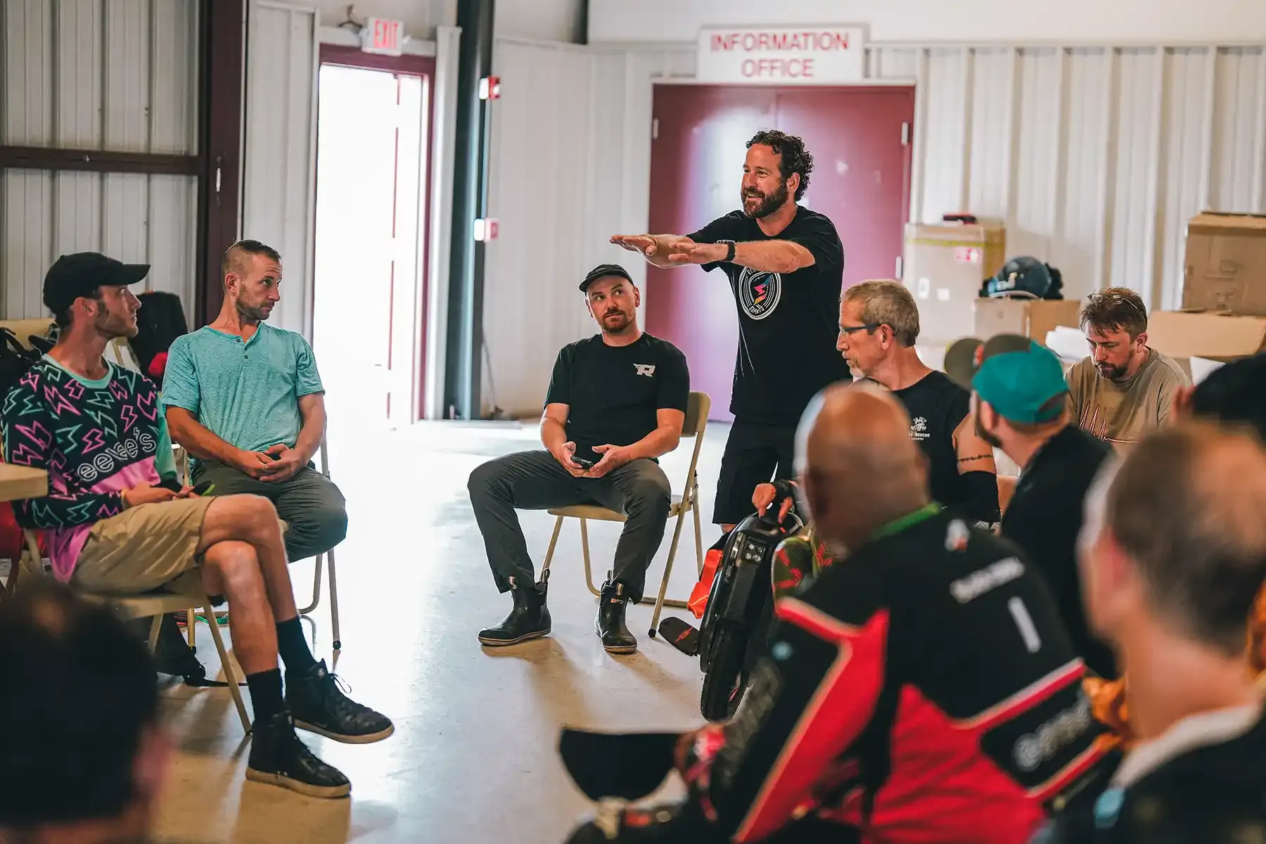 Riders sit in a circle at a workshop while an instructor explains